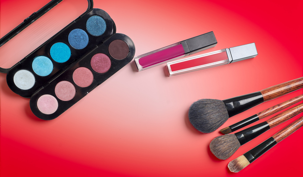 Блеск для губ, тени и кисточки на красном фоне