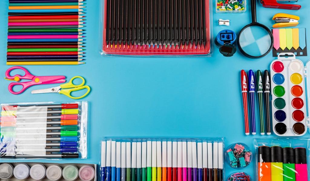 Много разноцветных канцелярских предметов на голубом фоне 