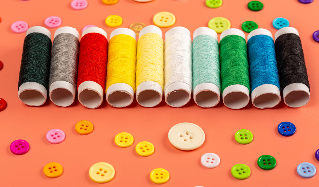 Разноцветные нитки и пуговицы на розовом фоне