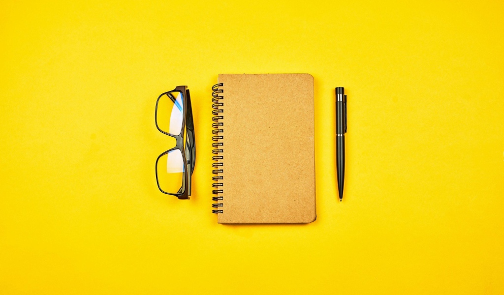 Notepad, glasses and pen on yellow background