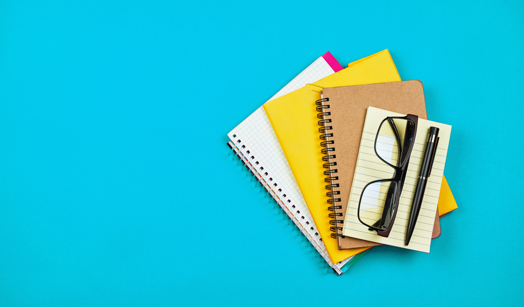 Блокноты, очки и ручка на голубом фоне