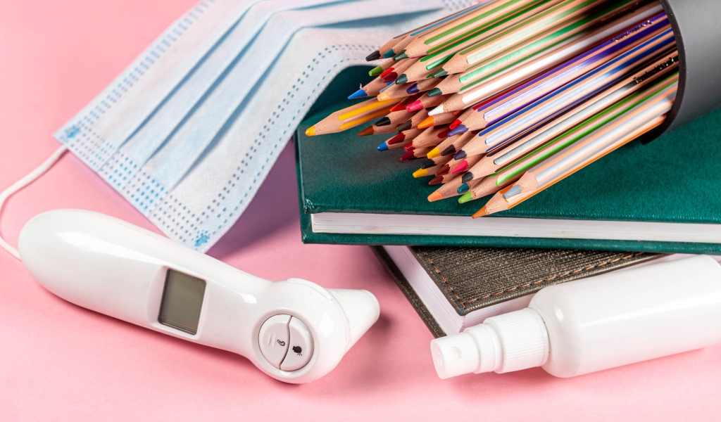 Карандаши, градусник, маска и блокнот на розовом фоне 