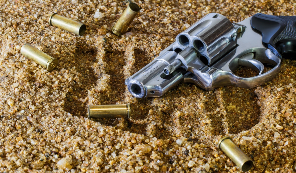 Револьвер с гильзами лежат на песке