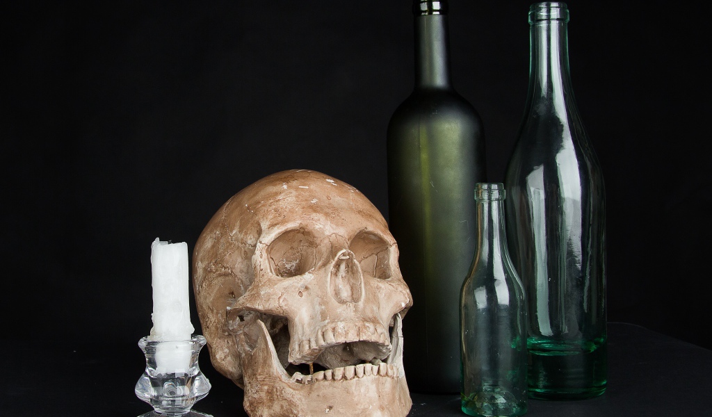 Череп, пустые бутылки и свеча на черном фоне