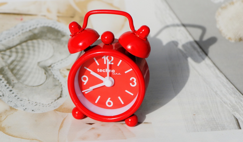 Маленький красный будильник стоит на столе 