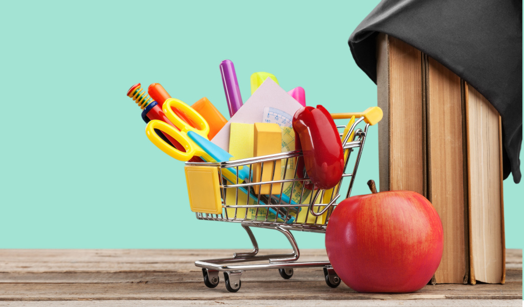 Канцелярские предметы в тележке на столе с яблоком и книгами 