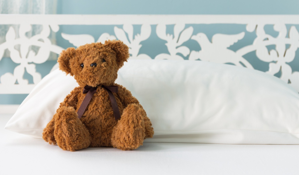 Игрушечный медвежонок сидит на белой постели