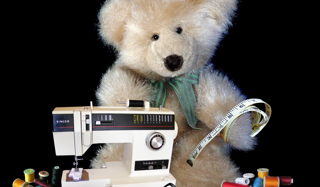 Игрушечный медвежонок со швейной машинкой на черном фоне 