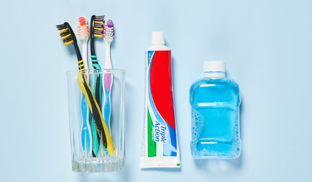 Зубная паста с щетками и ополаскивателем на сером фоне 