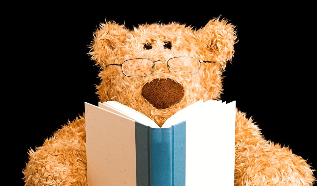 Игрушечный медведь в очках с книгой на черном фоне