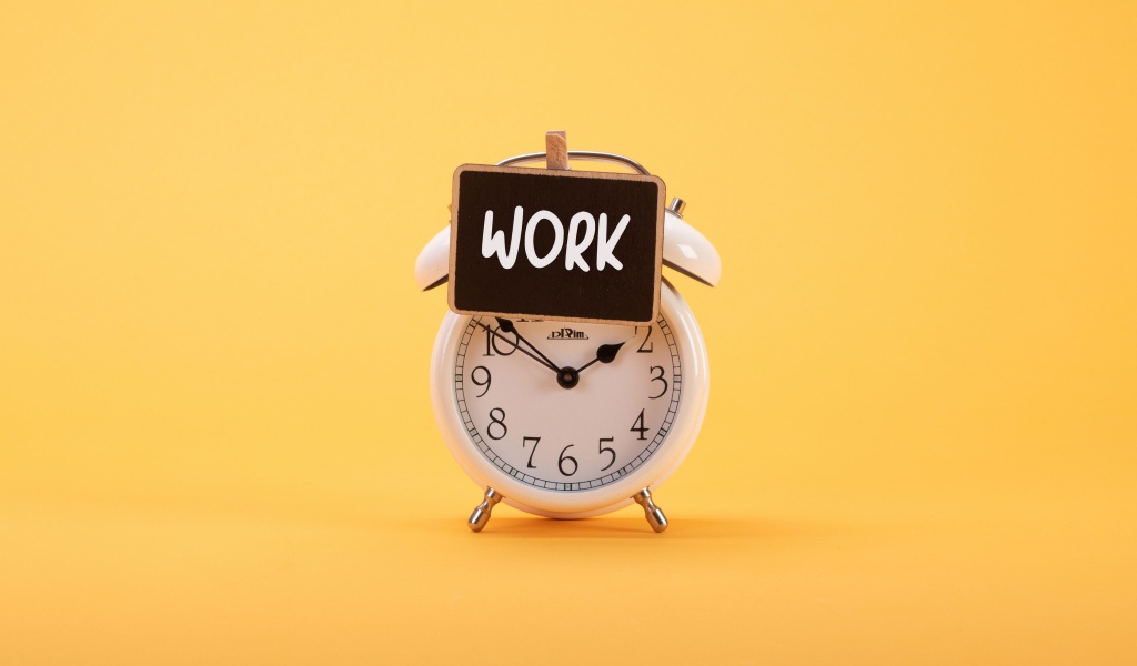 Белый будильник с табличкой на желтом фоне