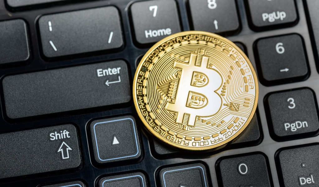 Золотая монета биткоин на черной клавиатуре