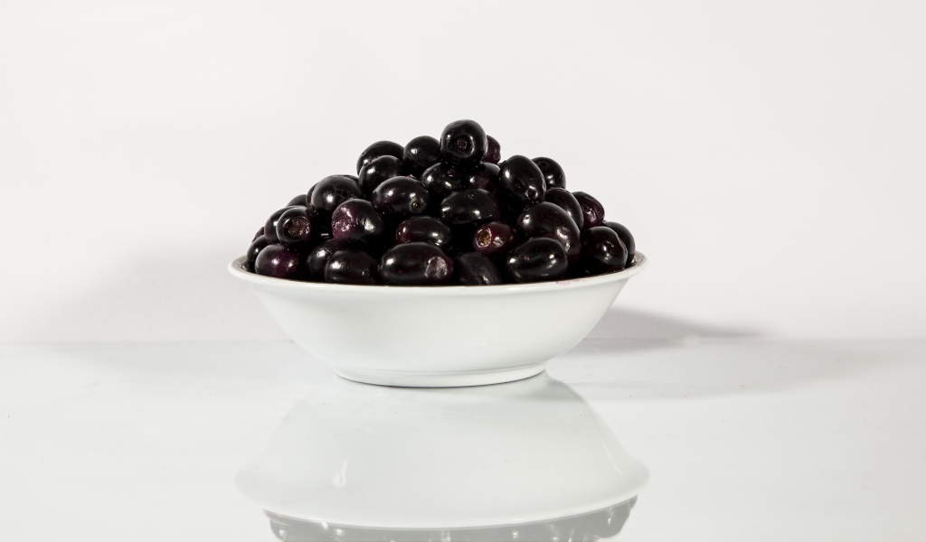 Черные оливки в белой тарелке отражаются в поверхности