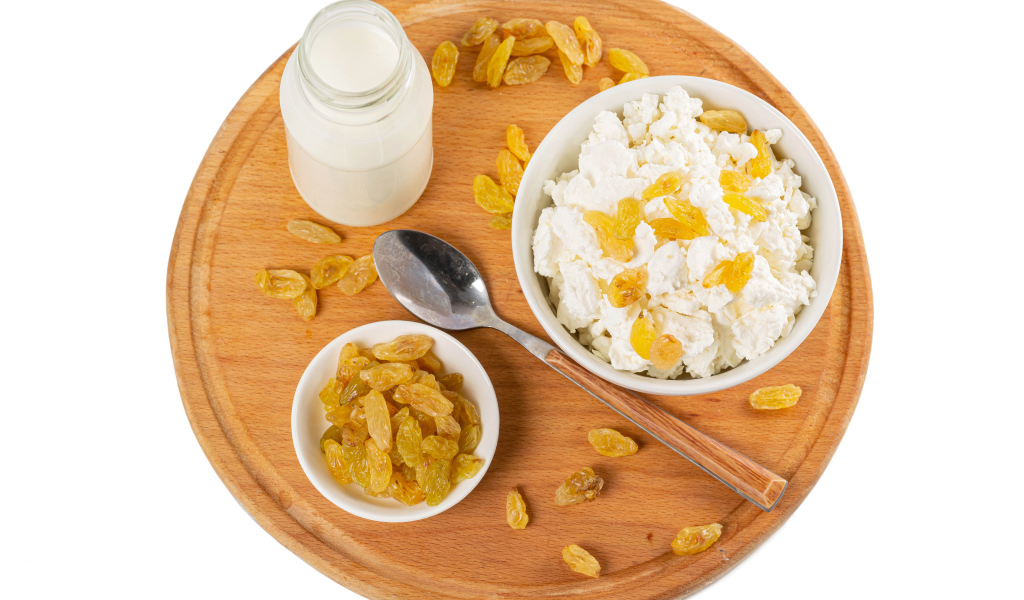 Творог с изюмом и молоком на доске на белом фоне 