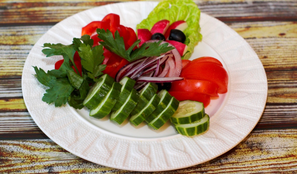 Свежие овощи на белой тарелке на деревянном фоне