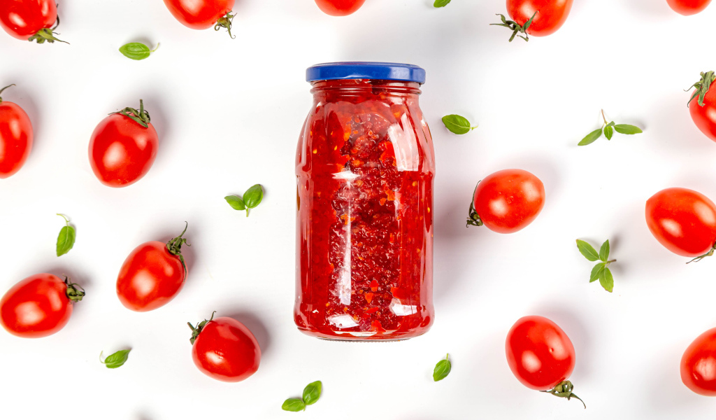 Банка аджики на белом фоне с помидорами