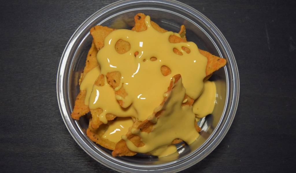 Чипсы начос с сырным соусом в миске на черном фоне