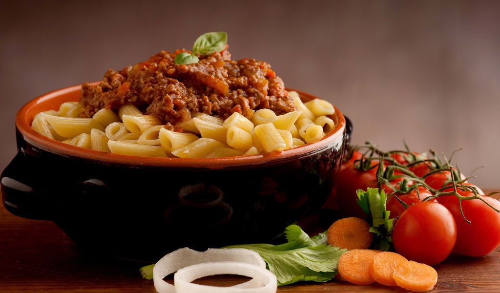 Макароны в миске с фаршем на столе с помидорами