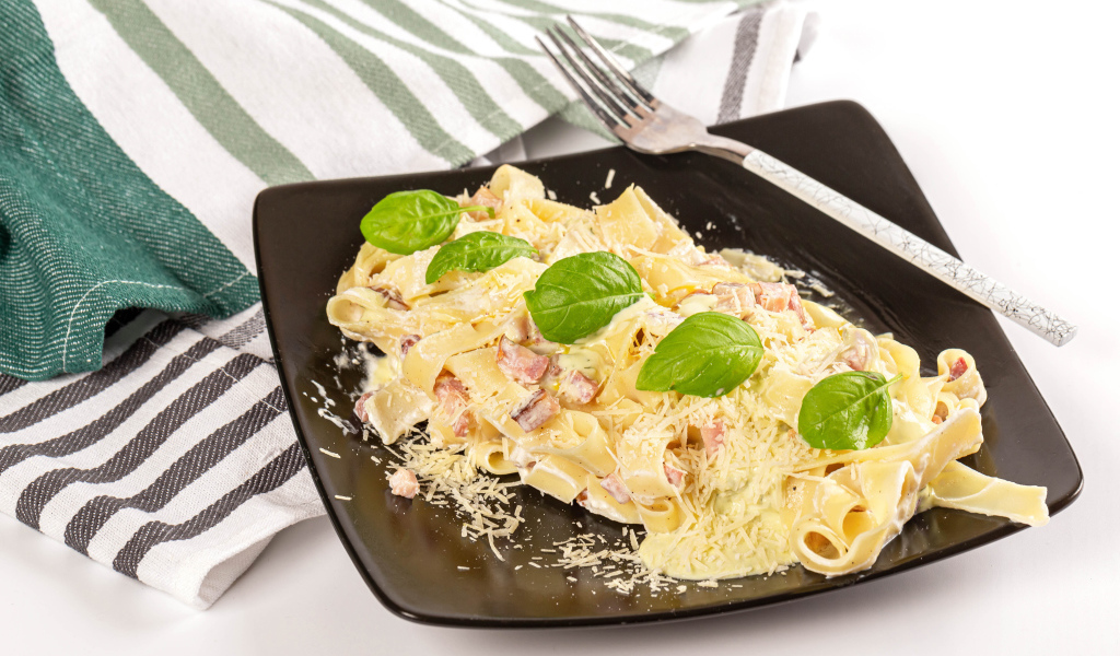 Макароны на тарелке с тертым сыром и кусочками мяса