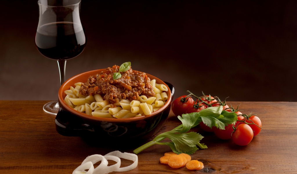 Макароны с фаршем на столе с бокалом вина и помидорами