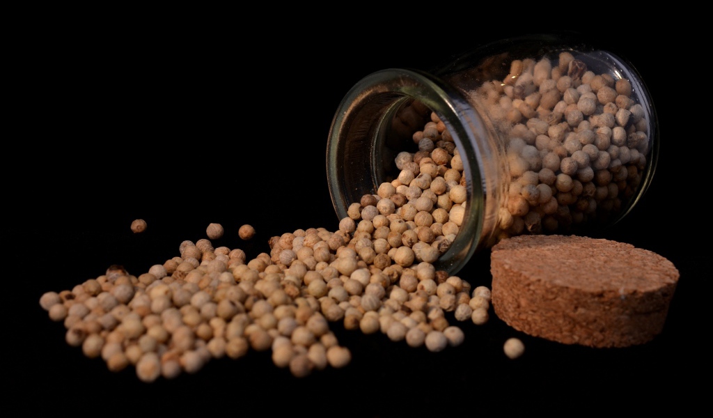 Перец горошек в стеклянной банке на черном фоне 