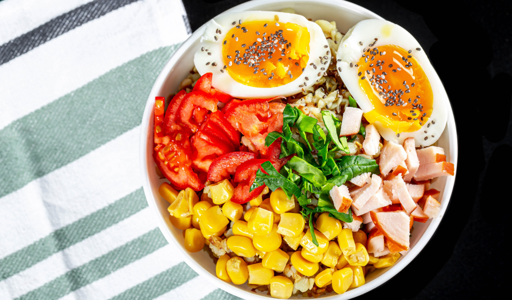 Каша в тарелке с помидорами, кукурузой, ветчиной и яйцом