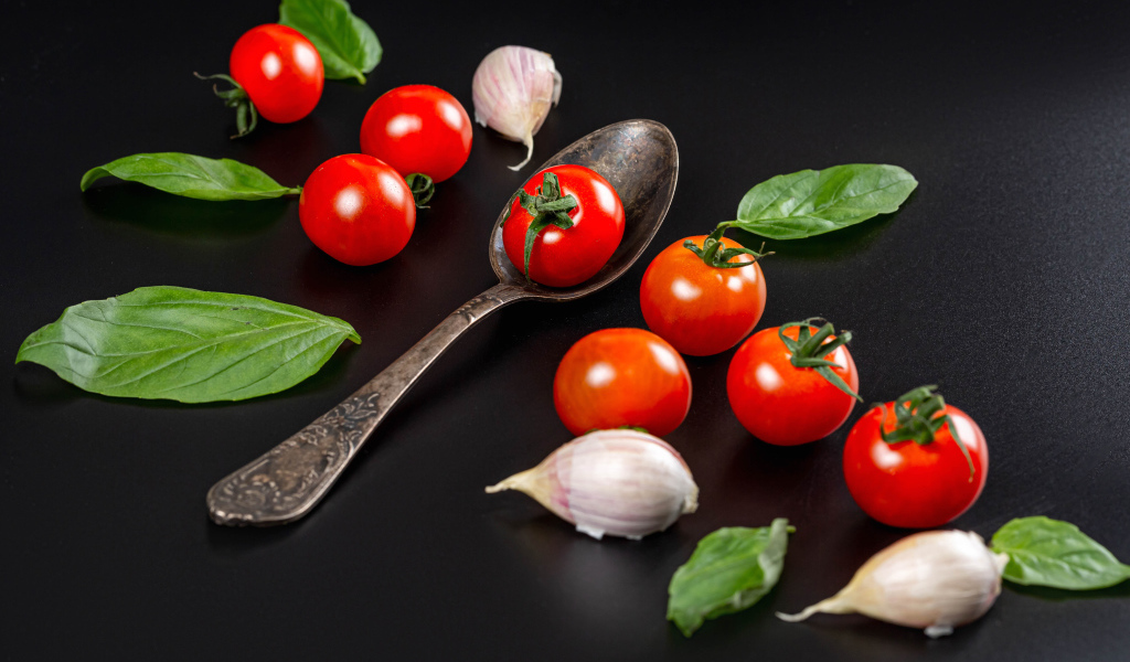 Красные помидоры с чесноком и листьями базилика на столе 