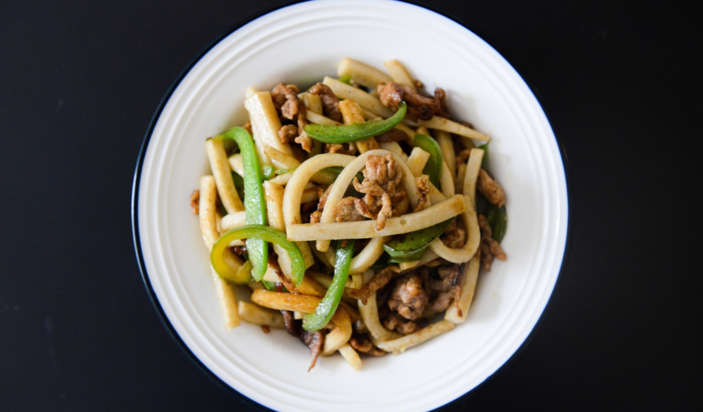 Салат с мясом в белой тарелке на черном фоне