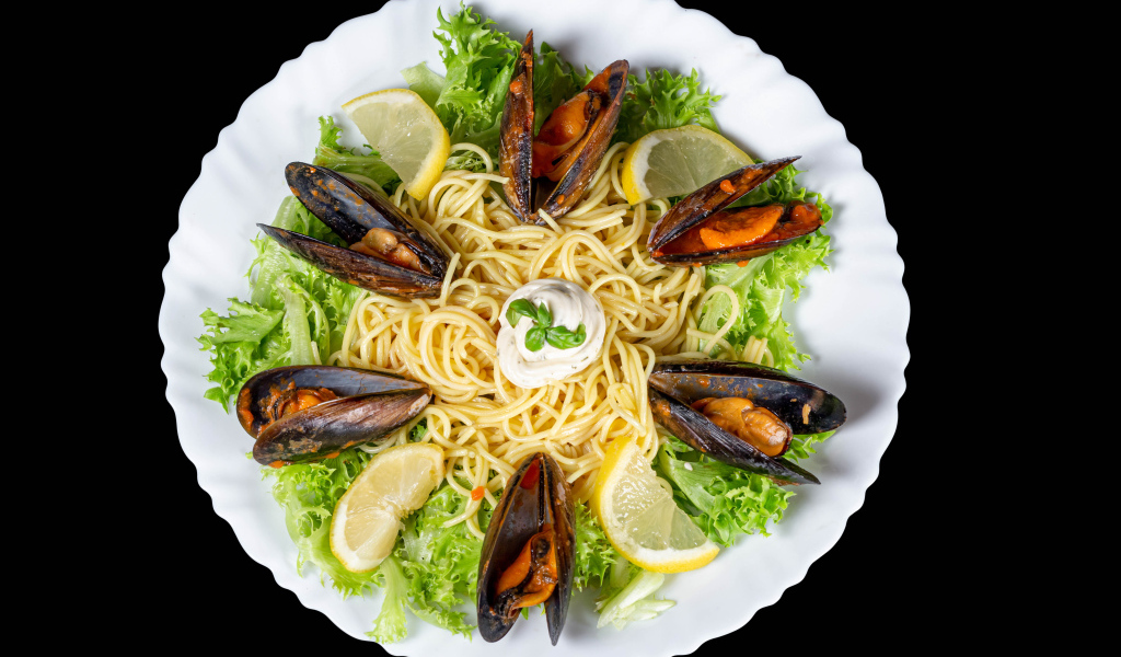 Спагетти с мидиями и листьями салата на белой тарелке