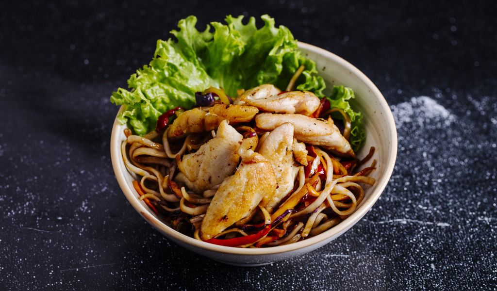 Спагетти с соусом в тарелке с кусочками курицы и листьями салата