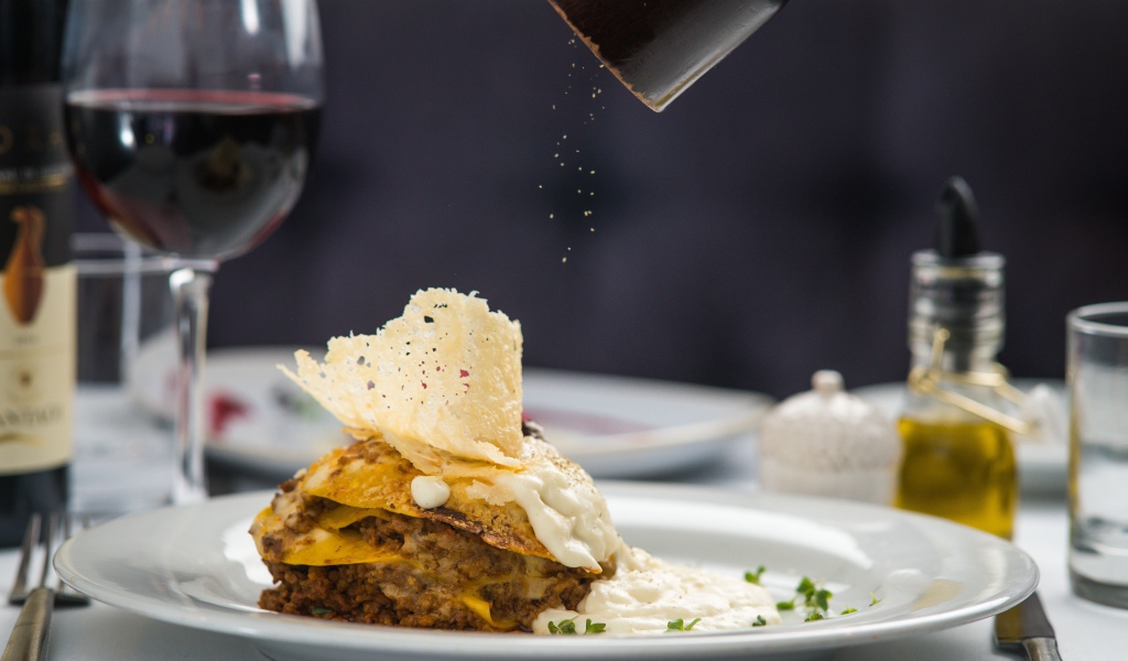 Кусок лазаньи посыпают перцем 