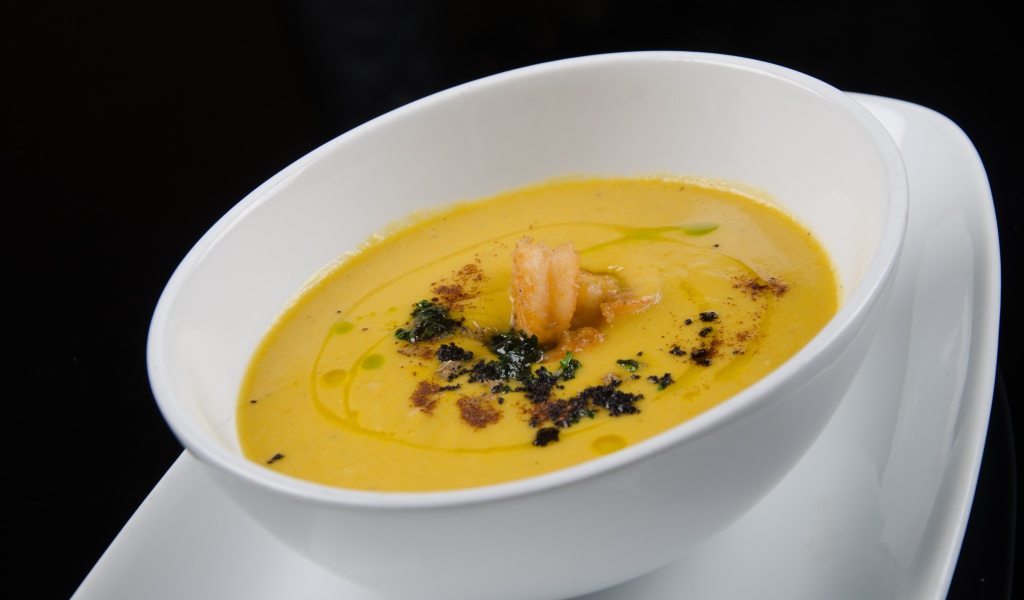Желтый суп пюре в белой тарелке на черном фоне