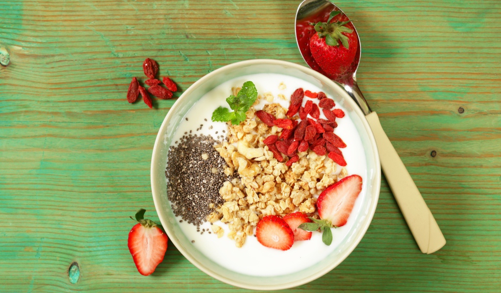 Йогурт с сухофруктами и клубникой на столе в миске 