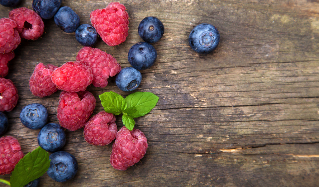 Голубые ягоды черники и красные ягоды малины на деревянном столе