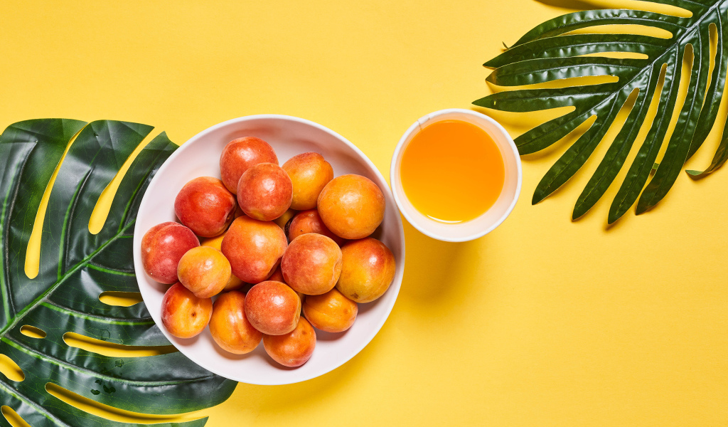 Вкусные спелые абрикосы с зелеными листьями на желтом фоне