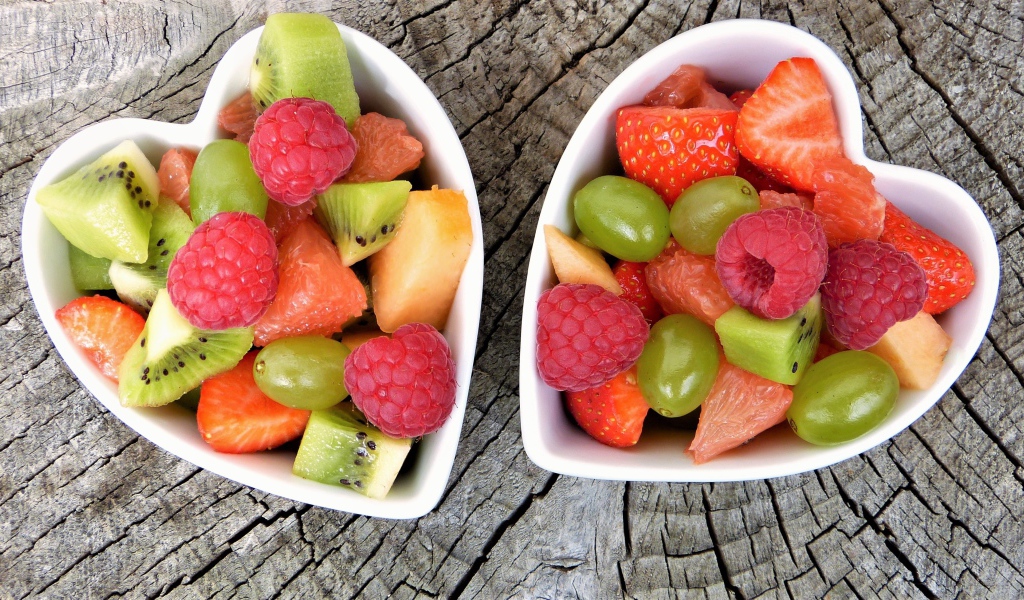 Салат из фруктов и ягод в белой тарелке на деревянном столе