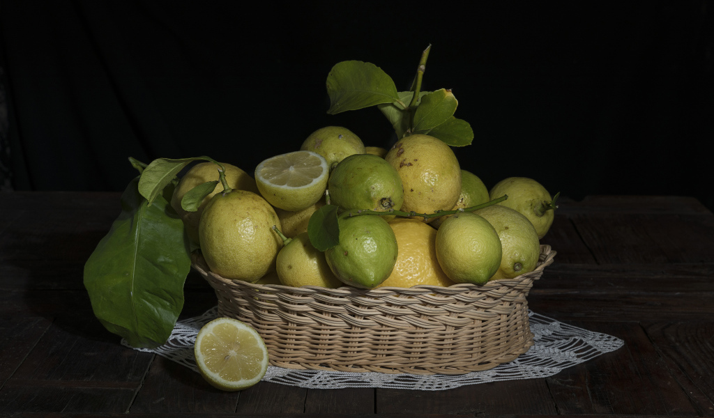Лимоны и лаймы в плетеной корзинке на черном фоне