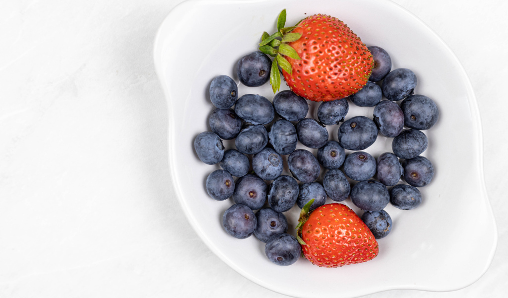 Много синей черники с клубникой в белой тарелке 