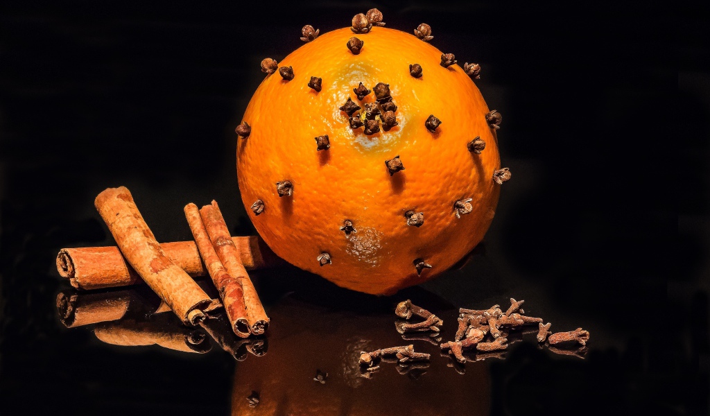 Оранжевый апельсин с гвоздикой и корицей на черном фоне 