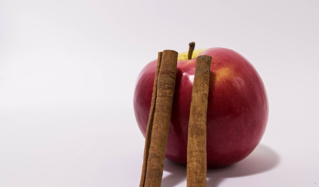 Красное яблоко с палочками корицы на сером фоне
