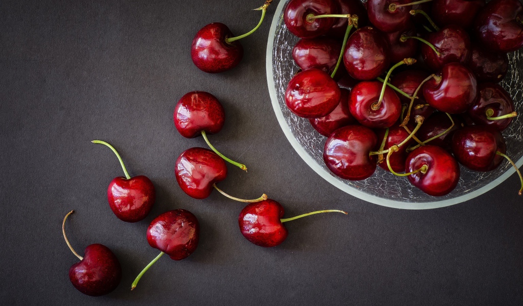 Красные черешни в миске на сером фоне