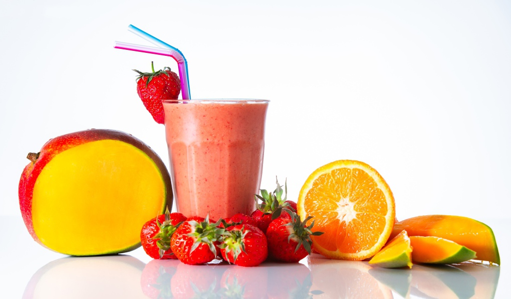 Спелое манго с клубникой и апельсином на столе со смузи