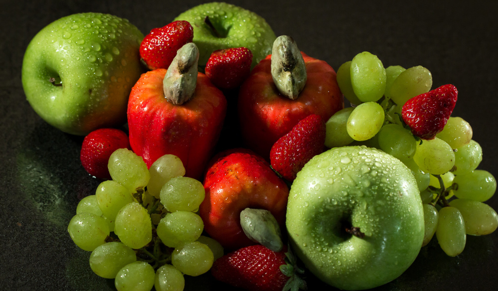 Мокрые яблоки, виноград и клубника на столе 