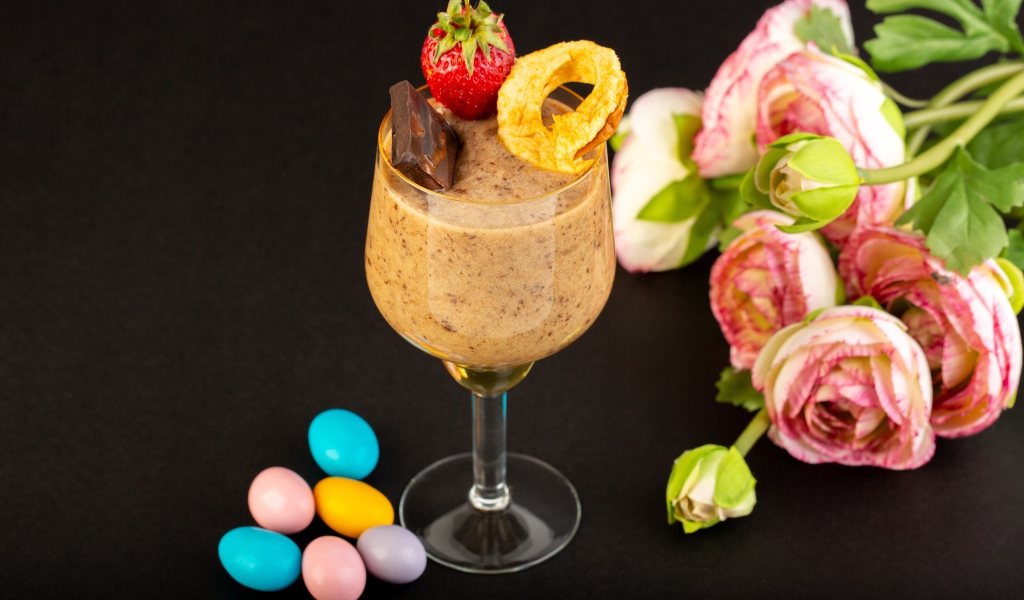 Коктейль с конфетами и букетом лютиков на черном столе