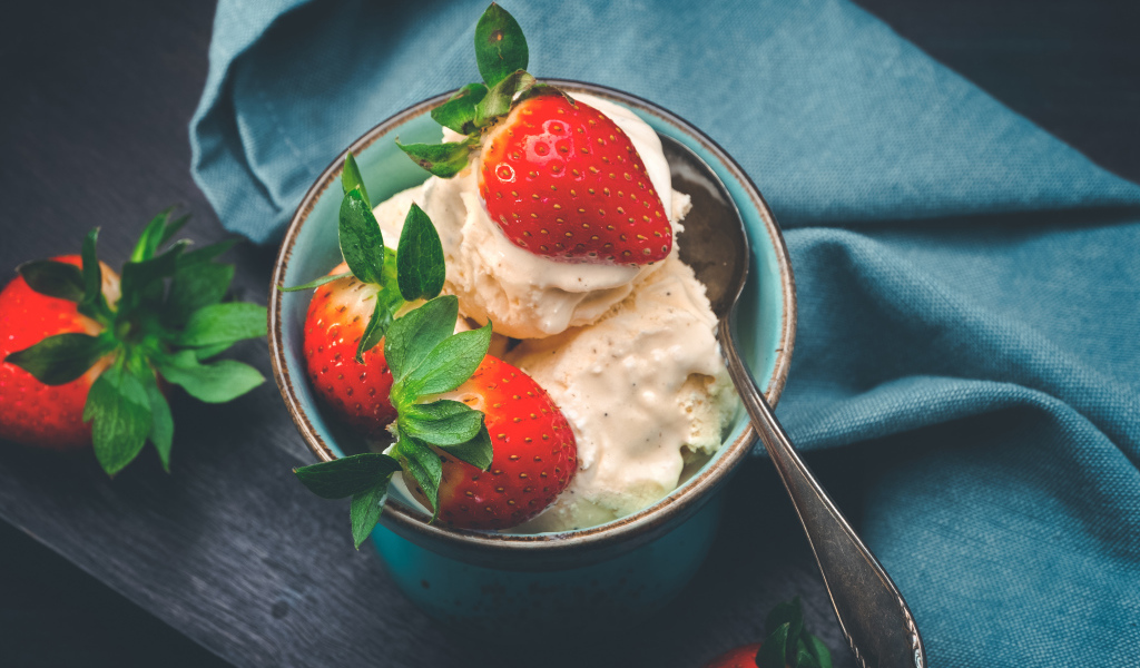 Сливочное мороженое с ягодами клубники в чашке с ложкой