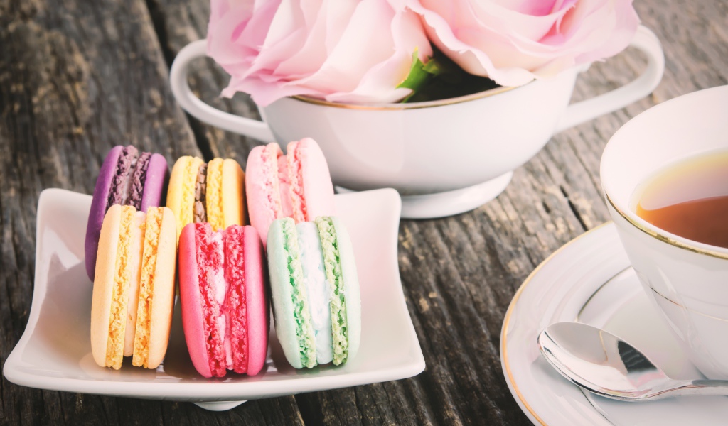 Десерт макарон на столе с чаем и цветами розы