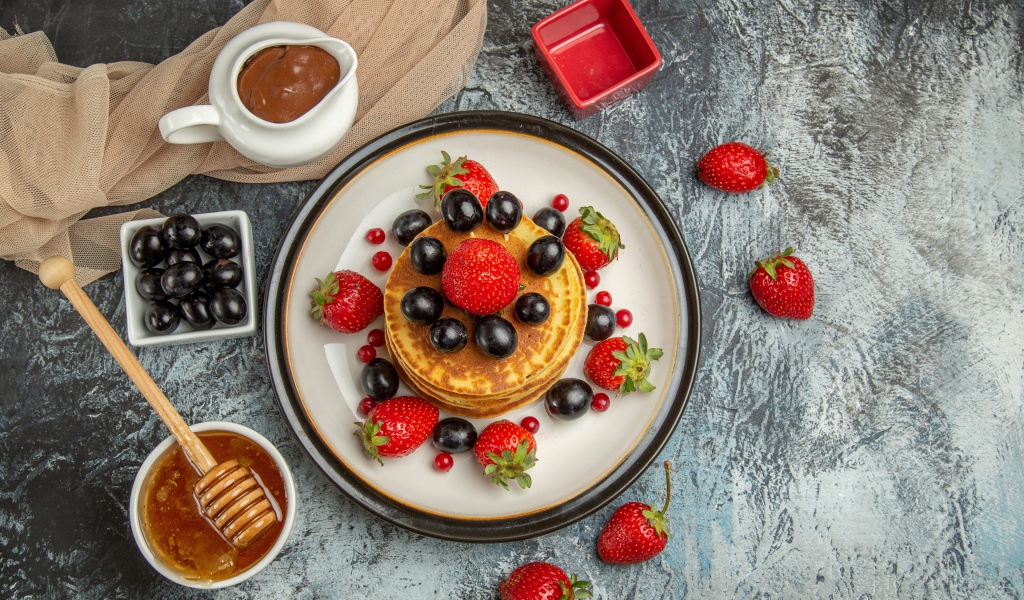 Оладьи с ягодами клубники и винограда на столе с медом