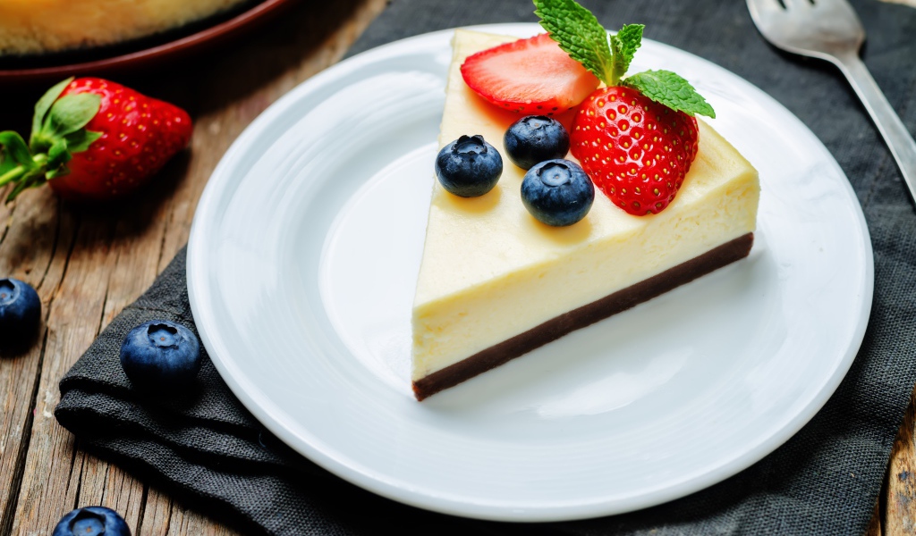 Кусок чизкейка на белой тарелке с клубникой и черникой 