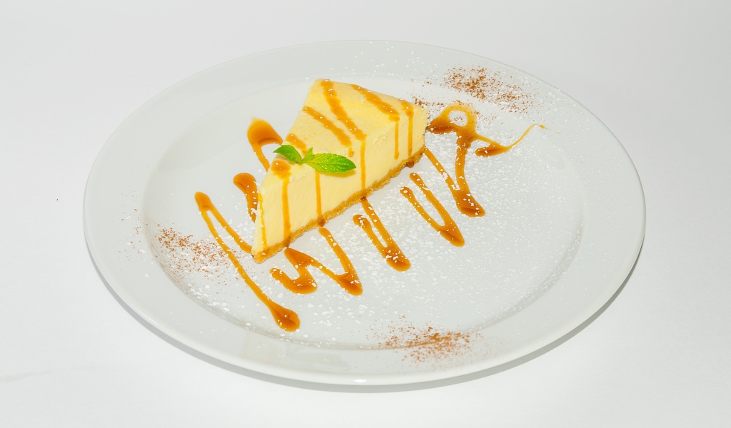 Кусок чизкейка с сиропом на большой белой тарелке 