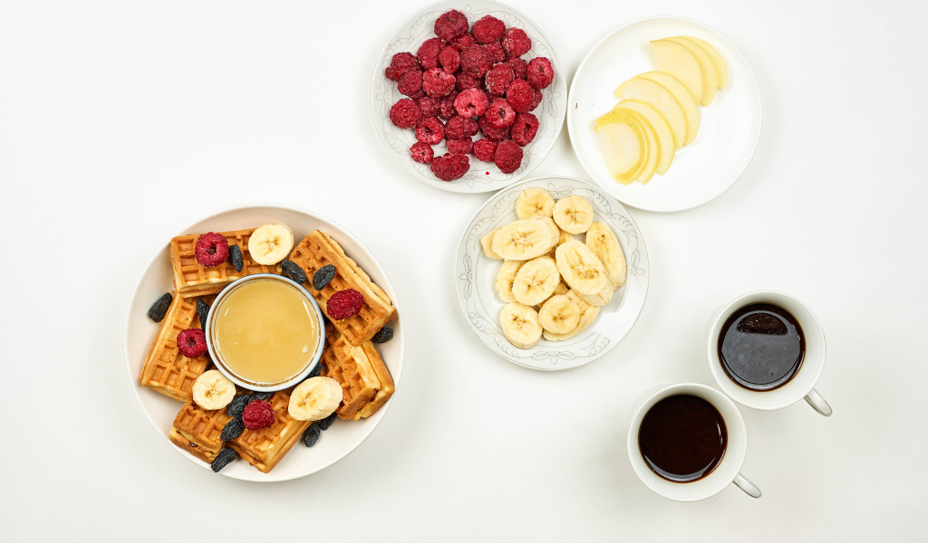Сладкие вафли с малиной и бананами на столе  с кофе